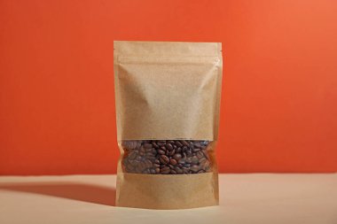 Kırmızı arka planda beyaz masada kahve çekirdekleri olan fermuarlı bir stand-up kesesi. Tasarım için model