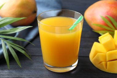 Bardakta lezzetli mango suyu, taze meyve ve ahşap masada yeşil yapraklar, yakın plan.