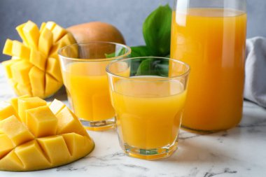 Bardakta lezzetli mango suyu, taze meyve ve yeşil yapraklar beyaz mermer masada, yakın plan.
