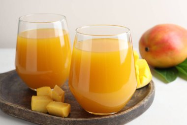 Bardakta lezzetli mango suyu, taze meyve ve yeşil yapraklar beyaz masada, yakın plan.