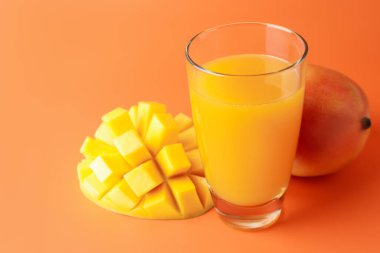 Bardakta lezzetli mango suyu ve turuncu arka planda taze meyve, yakın plan.