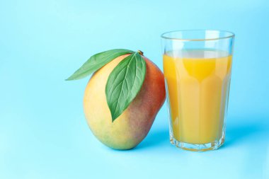 Bardakta lezzetli mango suyu ve açık mavi arka planda taze meyve.