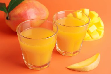 Bardakta lezzetli mango suyu ve turuncu arka planda taze meyve, yakın plan.