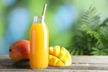 Cam şişedeki lezzetli mango suyu ve ahşap masadaki taze meyveler bulanık arka planda, mesaj için yer var.