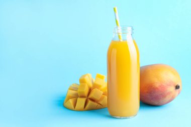 Cam şişede lezzetli mango suyu ve açık mavi arka planda taze meyve, mesaj için yer var.