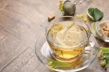 Fincanda taze ıhlamur çayı, şeker küpleri ve tahta masada çiçekler, yakın plan. Metin için boşluk