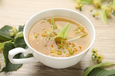 Fincanda taze ıhlamur çayı ve ahşap masada çiçekler, yakın plan.