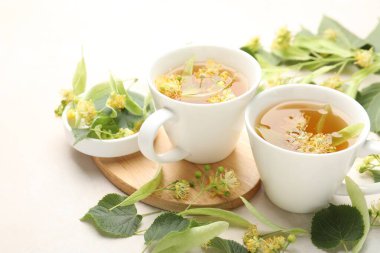 Fincanlarda taze ıhlamur çayı ve beyaz masada çiçekler, yakın plan.