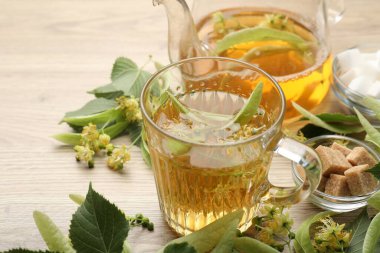 Taze ıhlamur çayı, çaydanlık, şeker küpleri ve çiçekler ahşap masada, yakın plan.