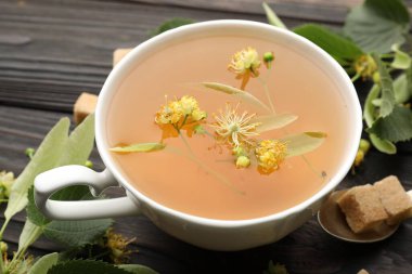 Taze ıhlamur çayı, şeker küpleri ve çiçekler koyu ahşap masada, yakın plan.