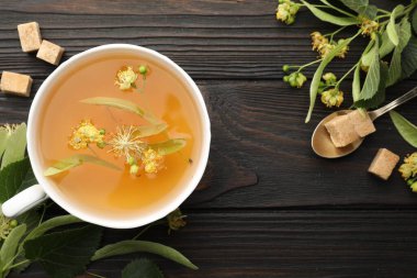 Fincanda taze ıhlamur çayı, şeker küpleri ve koyu ahşap masa üzerinde çiçekler, düz uzanma. Metin için boşluk