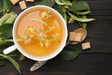 Taze ıhlamur çayı, şeker küpleri ve çiçekler koyu ahşap masada, düz uzanmış