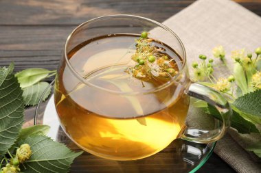 Fincanda taze ıhlamur çayı ve koyu ahşap masada çiçekler, yakın plan.