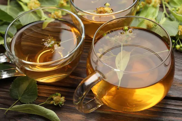 Fincanlarda taze ıhlamur çayı ve ahşap masada çiçekler, yakın plan.