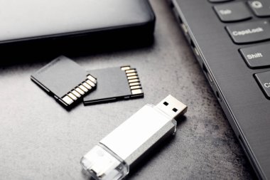 SD hafıza kartları, USB flash disk, sabit disk ve koyu gri masadaki dizüstü bilgisayar, yakın plan.