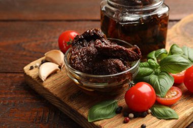 Lezzetli güneşte kurutulmuş domatesler, taze sebzeler, fesleğen ve sarımsak ahşap masada, yakın plan.