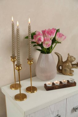 Mumları yanan zarif şamdanlar vazoda laleler ve bej duvarın yanındaki şifoniyerde diğer dekorlar.