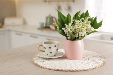 Vadideki güzel zambak buketi ve mutfaktaki ahşap masada duran kupa.