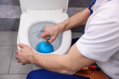 Tesisatçı tuvalet tıkanıklığını açıyor, içeride pompa var, yakın plan.