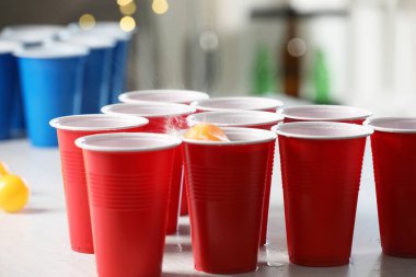 Aydınlık masada, bulanık ışıklara karşı plastik bardağa düşen turuncu top. Bira pong oyunu
