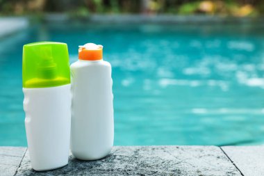 Dışarıdaki yüzme havuzunun yakınındaki taş yüzeyde güneş koruma ürünleri şişeleri, metin için yer.