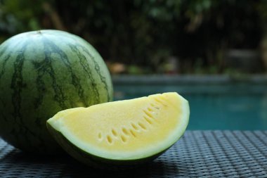 Açık havuz kenarında hasır masada sarı karpuzlar var. Yakın plan. Metin için boşluk