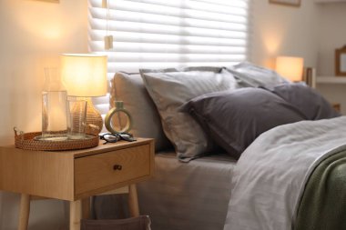 Yumuşak çarşaflı, komodinli ve lambalı rahat bir yatak. Ev tekstili