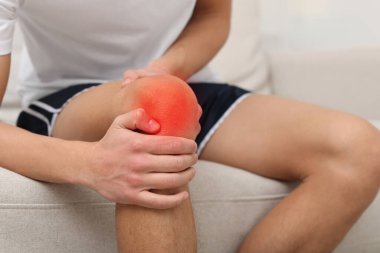 Evdeki koltukta dizinde ağrıdan muzdarip bir adam, yakın plan.