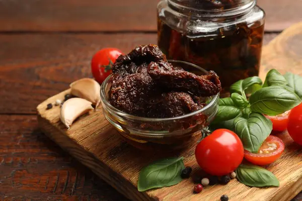 Lezzetli güneşte kurutulmuş domatesler, taze sebzeler, fesleğen ve sarımsak ahşap masada, yakın plan.