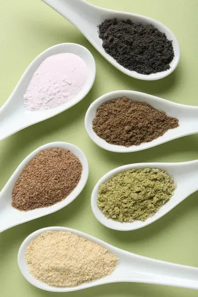 Farklı süper yiyecek tozları soluk yeşil arka planda kaşıklarda, düz yerde.
