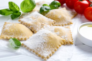 Pişmemiş ravioli, fesleğen, domates ve yağ beyaz ahşap masada, yakın plan.