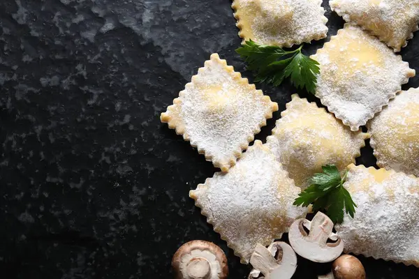 Pişmemiş ravioli, maydanoz ve mantarlar siyah masada, düz yerde. Metin için boşluk
