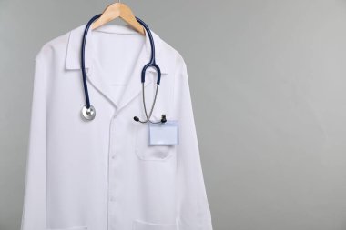 Üzerinde steteskop ve rozet olan doktor ceketi gri arka planda. Metin için boşluk