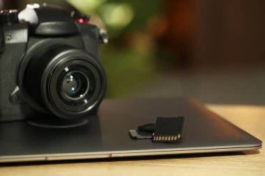 SD hafıza kartları, dizüstü bilgisayar ve fotoğraf makinesi ahşap masada, yakın plan.