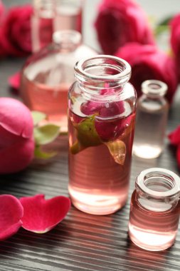 Aromatik esanslı parfüm şişelerini aç ve gri ahşap masada güller, yakın plan.