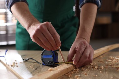 İçerideki ahşap masada bant ve kalemle tahta ölçen adam, yakın plan.