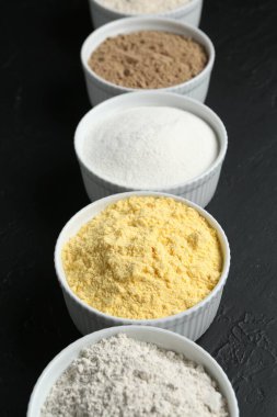 Siyah desenli masa üzerindeki kaselerde farklı un türleri, yakın plan.