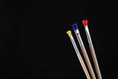 Siyah arka planda renkli üç fırça, yakın plan. Metin için boşluk