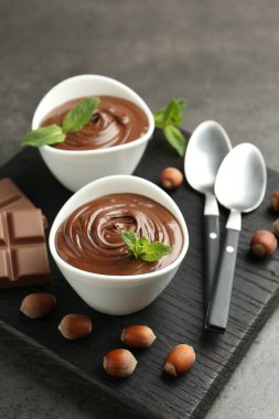 Lezzetli çikolata, parçalar, nane ve fındıklar gri masada, yakın plan.