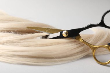 Açık gri arka planda makasla sarı saç tokası kesiliyor. Yakın plan.