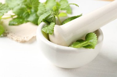 Taze limon merhemi yaprakları ve beyaz ahşap masada havan topuzu, yakın plan.