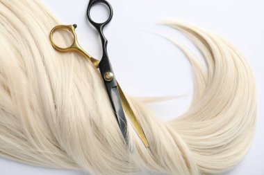 Beyaz zemin üzerinde saç kilidi ve makas düz yatar