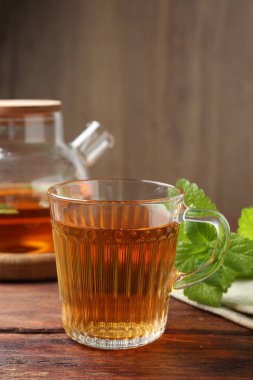 Cam fincanda aromatik limon merhemi çayı, çaydanlık ve ahşap masada taze yapraklar.