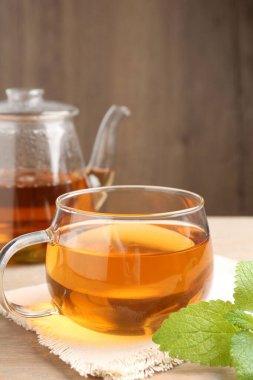 Cam bardakta Aromatik limon merhemi çayı, çaydanlık ve taze yapraklar masada, yakın plan.
