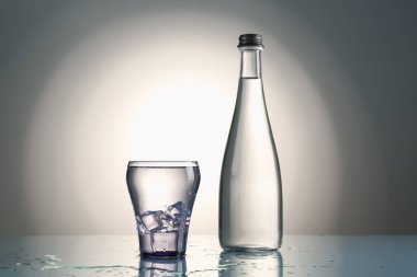 Taze su, cam küplerde buz ve ayna masasının üzerinde gri gradyan arka planda duran şişe.