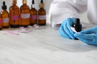 Laboratuvarda beyaz ahşap masada lüks parfüm üreten profesyonel bir parfümcü.