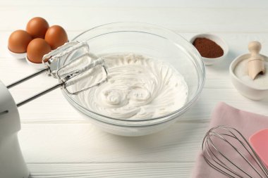 Krem şantili kase, el çırpıcı, çırpıcı ve malzemeler beyaz ahşap masada, yakın plan.