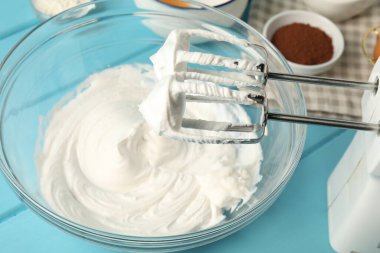 Krem şantili kase, el çırpıcı ve malzemeler açık mavi ahşap masada, yakın plan.