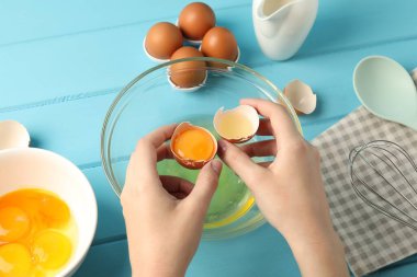 Açık mavi ahşap masada yumurta sarısını beyaz cam kaseden ayıran kadın.