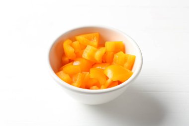 Beyaz ahşap masada kasede taze turuncu dolma biber parçaları, yakın plan.